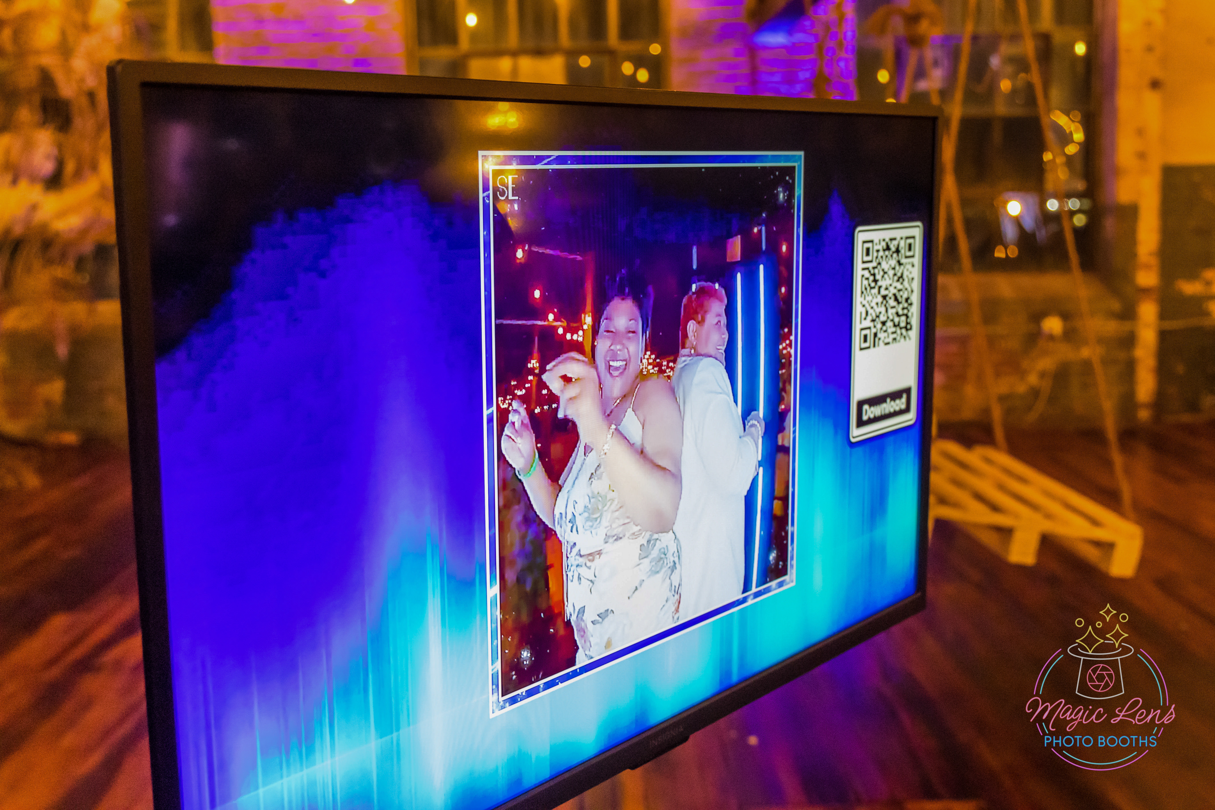 A photo preview with a Qr code on the big screen tv of two pretty ladies photo taken on the 360 photo booth